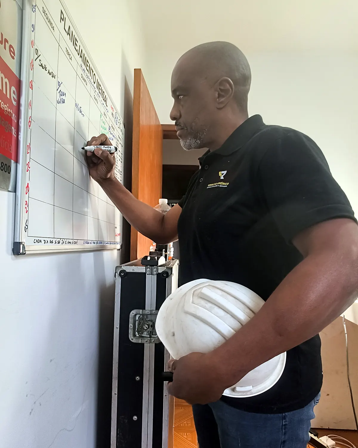 Ronaldo Américo planejando serviço elétrico no quadro branco, com capacete de segurança