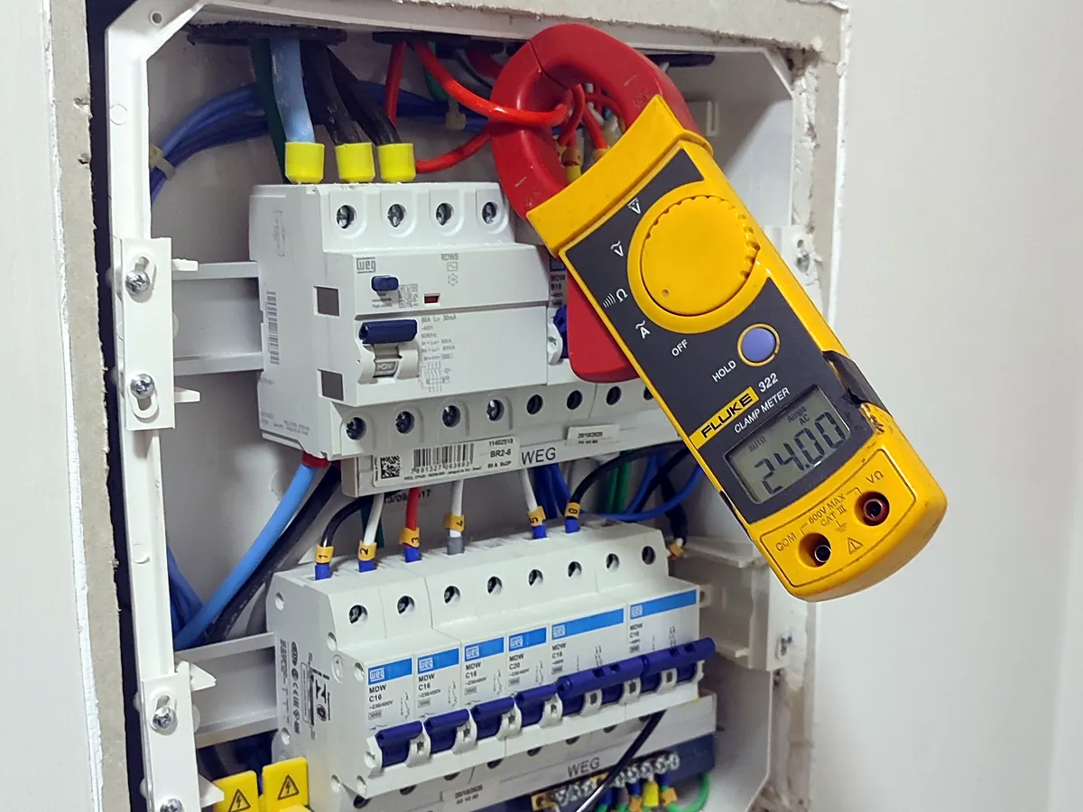 Medição de corrente com alicate amperímetro em quadro de distribuição durante inspeção elétrica
