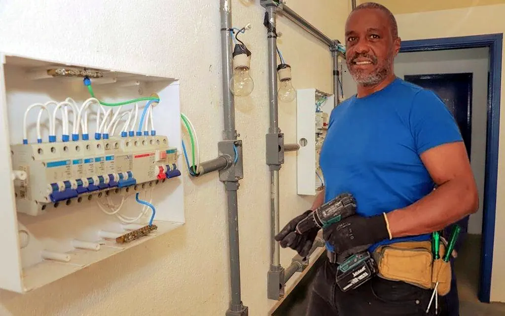 Eletricista Ronaldo Américo ao lado de quadro de distribuição montado com disjuntores